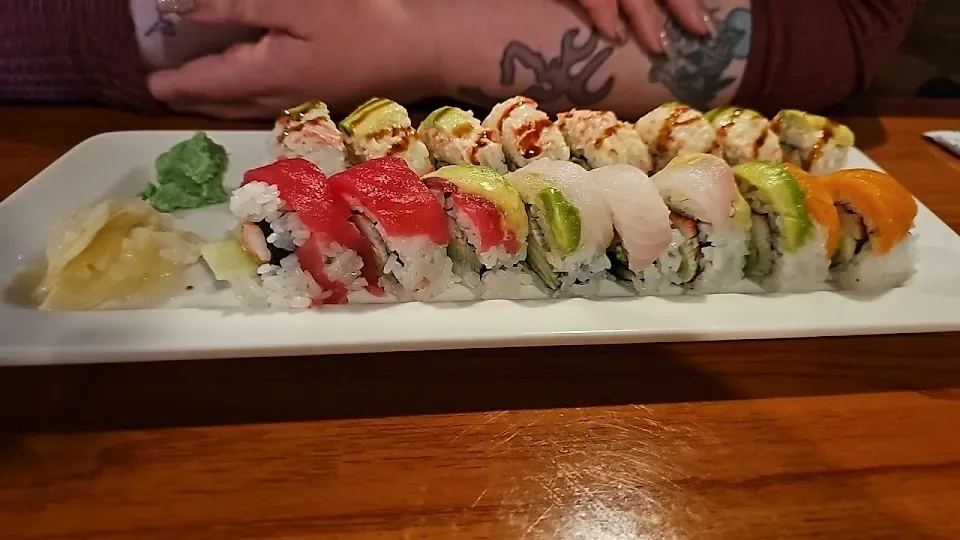 Long white plate of sushi rolls topped with tuna, salmon and avocado